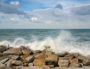 wave-crushing-concrete-breakwater-on-the-beach-over-blue-sky-at-day-picture-id1043078070